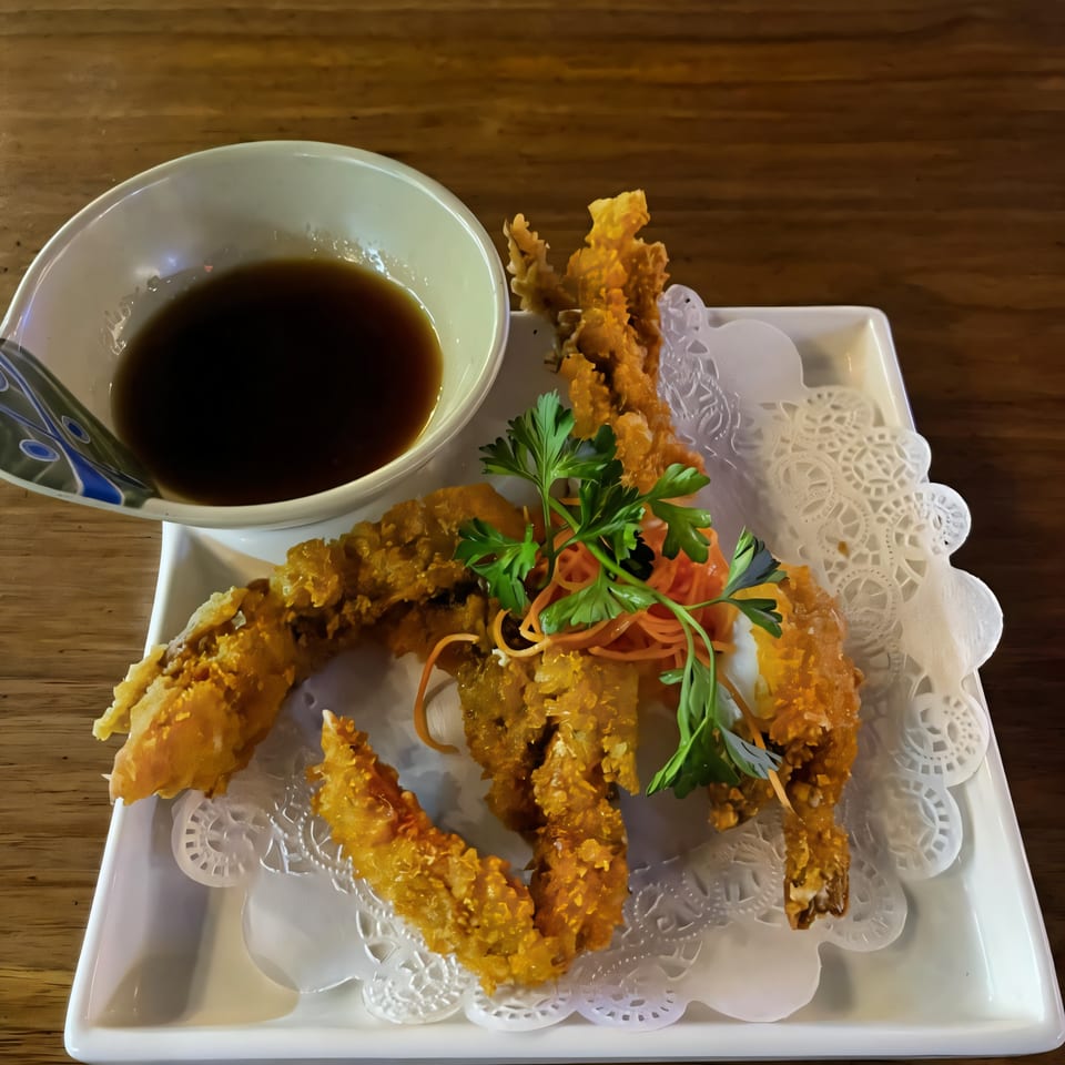 Crispy fried soft-shell crab tempura, garnished with parsley and shredded carrots, served with a dipping sauce.